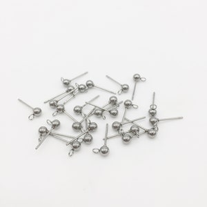 May include: A pile of silver-toned earring posts with small round balls on the ends. The posts are scattered on a white surface.