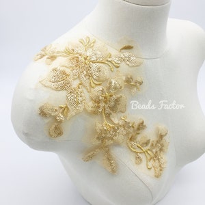 May include: Gold floral applique with sequins and beads on a white background. The applique is ideal for adding a touch of elegance to any garment.