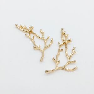May include: Two gold-colored metal branch-shaped charms. The charms are delicate and intricate, with multiple branches and twigs.