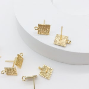 May include: Gold square earring findings with a textured surface and a loop for attaching a charm or pendant.