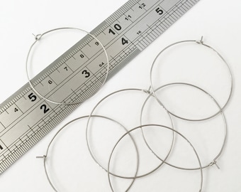 May include: Five silver hoop earrings of different sizes, measured against a ruler. The largest hoop measures 3 inches in diameter.