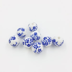 May include: A group of eight white ceramic beads with blue floral designs. The beads are round and have a smooth surface.