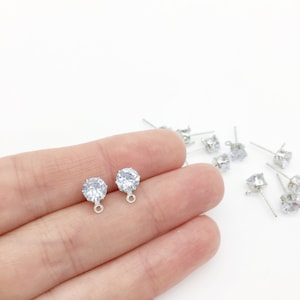 Könnte beinhalten: Ein Paar silberne Ohrring-Verschlüsse mit klaren runden Strasssteinen und einer silbernen Öse.