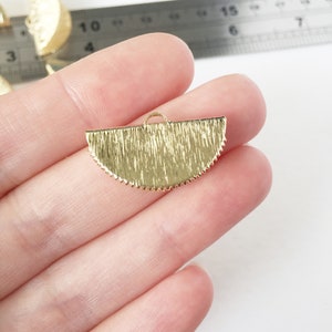 May include: Gold-toned metal half-circle pendant with a textured surface and a small loop at the top.
