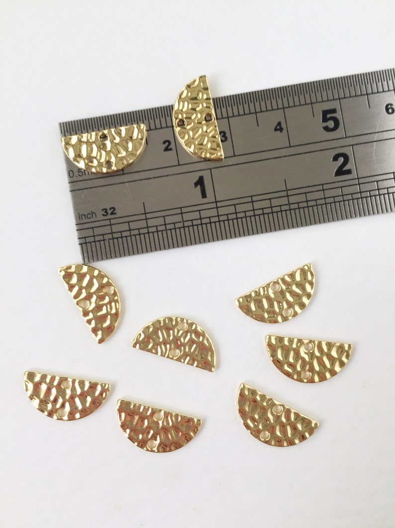 May include: Eight gold-toned metal half-circle charms with a hammered texture and two holes. The charms are approximately 1 inch in diameter.