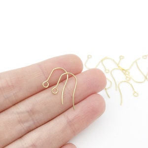 Könnte beinhalten: Goldfarbene Ohrringhaken, eine Nahaufnahme von mehreren Ohrringhaken in einer Hand, die Haken sind aus dünnem Metall und haben eine kleine Schlaufe oben.