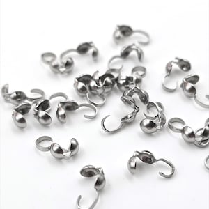 May include: A close-up of a pile of silver-toned metal clasps. The clasps are designed to be used for jewellery making and have a small hook on one end and a ball on the other.