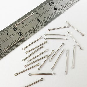 Peut inclure: Gros plan d'une règle mesurant 35,5 cm, avec 17 connecteurs métalliques argentés éparpillés autour. Les connecteurs mesurent environ 2,5 cm de long et ont une boucle à chaque extrémité.