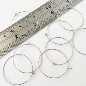May include: Five silver hoop earrings of varying sizes, measured against a ruler. The largest hoop measures 10 cm in diameter.