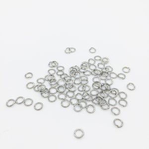 May include: A pile of silver jump rings on a white background. The rings are small and round, and they are ideal for jewellery making.