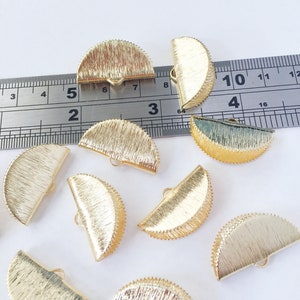 May include: Ten gold-coloured metal half-circle embellishments with a textured surface and a small loop on the back. The embellishments are approximately 2.5 cm in diameter.