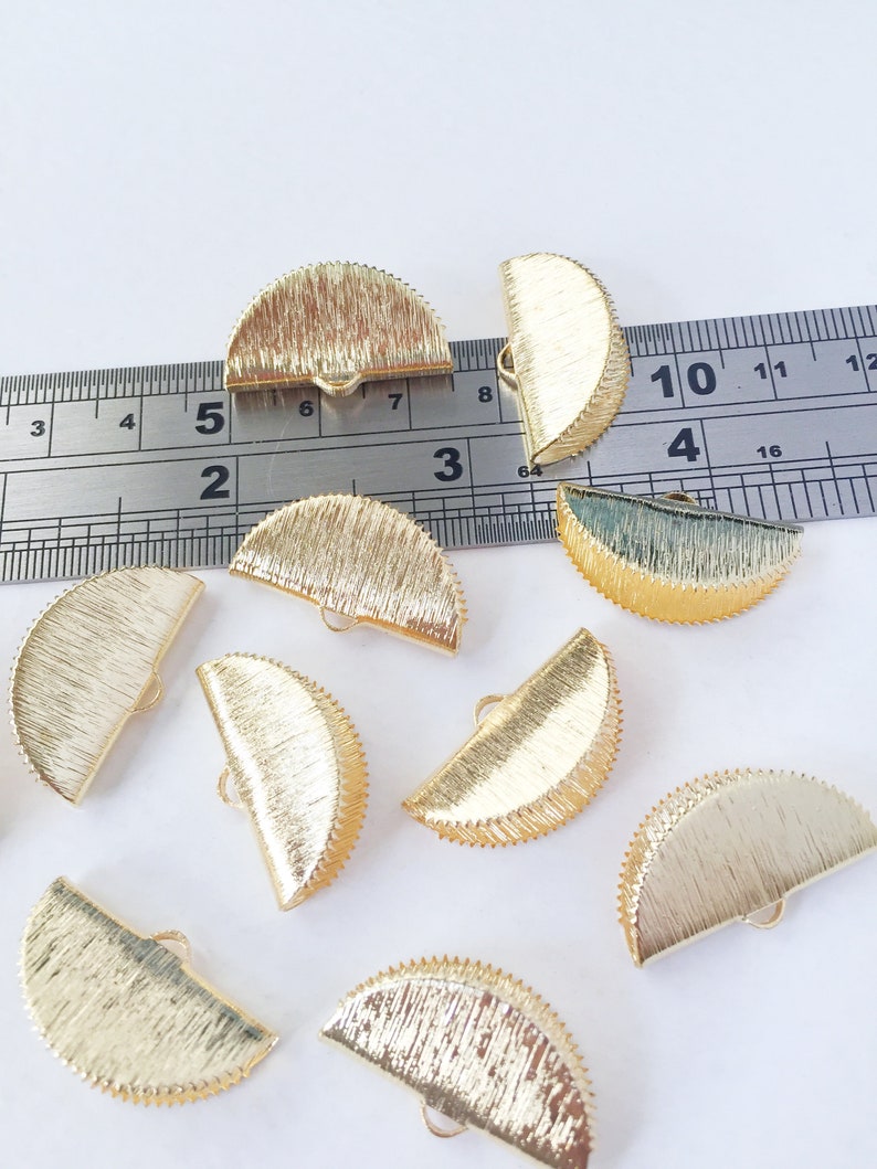 May include: Ten gold-coloured metal half-circle embellishments with a textured surface and a small loop on the back. The embellishments are approximately 2.5 cm in diameter.