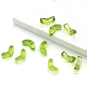 May include: A collection of ten green glass beads in the shape of a crescent moon. The beads are scattered on a white surface.