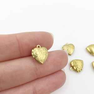 May include: Gold heart-shaped locket charms with a floral design. The lockets are small and have a loop at the top for attaching to a necklace or bracelet.
