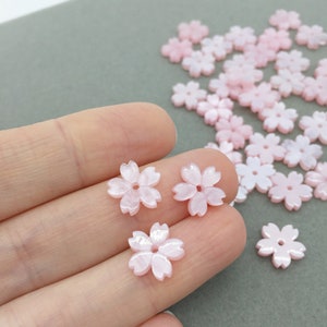 May include: Pink and white shell flower beads with a five-petal design. The beads are approximately 1 cm in diameter and have a pearlescent finish.
