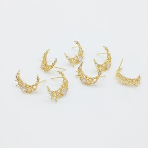 May include: Six gold crescent moon earrings with clear crystal embellishments. The earrings are arranged in a semi-circle on a white background.