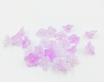 May include: A scattering of iridescent purple flower-shaped beads on a white background.
