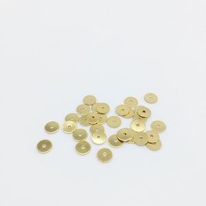 May include: A pile of small, round, gold-colored metal discs. The discs have a smooth, slightly textured surface.