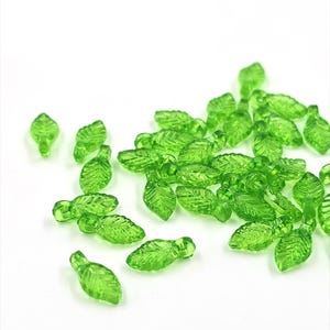 May include: A scattering of green glass leaf-shaped beads. The beads are translucent and have a slightly textured surface.