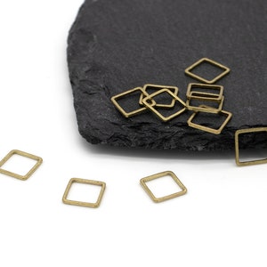 Könnte beinhalten: Ein Haufen goldfarbener quadratischer Sprungringe auf einer schwarzen Schieferoberfläche. Auf einer weißen Oberfläche liegen vier weitere Sprungringe.