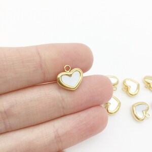 May include: Gold heart-shaped charms with a white centre. The charms have a small loop at the top for attaching to jewellery or other crafts.