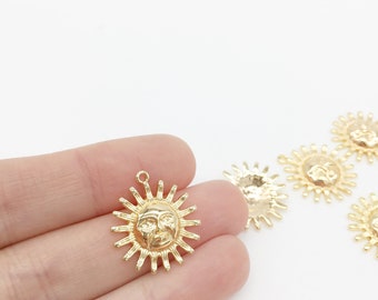 Könnte beinhalten: Goldfarbener Metall-Sonnenanhänger mit einem Gesicht und Strahlen. Der Anhänger wird auf einer Hand vor weißem Hintergrund gezeigt.