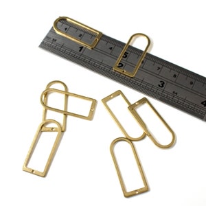 May include: A set of six gold-toned metal rectangular frames with rounded corners and a small hole at the top. The frames are arranged on a white surface with a ruler in the background.