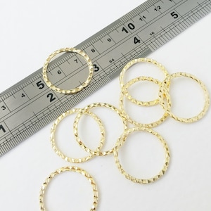 May include: Eight gold-coloured metal jump rings with a textured diamond pattern. The rings are approximately 2.5 cm in diameter.