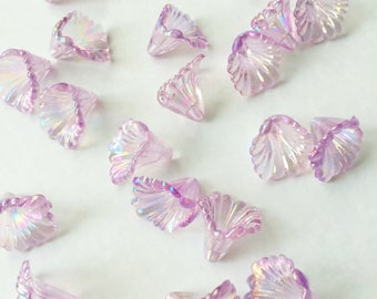 May include: A collection of iridescent purple flower-shaped beads. The beads are made of glass and have a scalloped edge. They are scattered on a white surface.