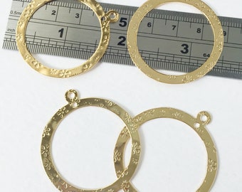 Peut inclure: Quatre cercles en métal de couleur dorée avec un motif floral. Chaque cercle a une petite boucle en haut. Les cercles sont mesurés avec une règle en centimètres.