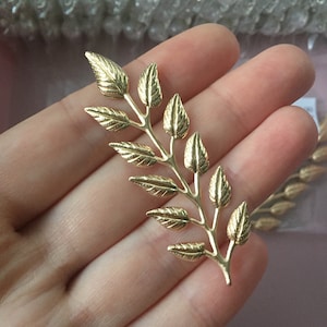 Könnte beinhalten: Goldene Blattzweige mit detaillierten Blättern. Der Zweig ist aus Metall und hat eine glänzende Oberfläche.