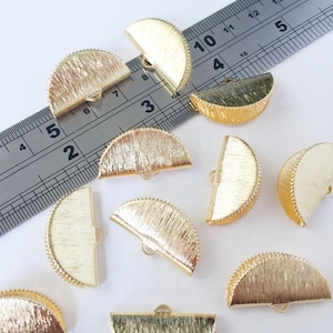 May include: Ten gold-coloured metal half-circle embellishments with a textured surface and a small loop on the top. The embellishments are scattered on a white surface.