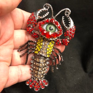 Broche artístico peculiar e extravagante em forma de olho de lagosta ou lagostim, com um olho verde natural, strass colocados à mão e uma cauda ARTICULADA!