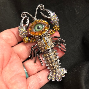 Broche artístico peculiar e extravagante em forma de olho de lagosta ou lagostim, com um olho verde natural, strass colocados à mão e uma cauda ARTICULADA!