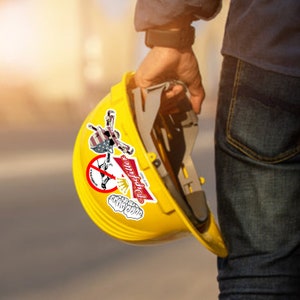 May include: A yellow hard hat with a sticker that says "Do It Yourself" and a sticker with an American flag and a skull. The sticker also says "Don't Panic It's Just a Sticker".