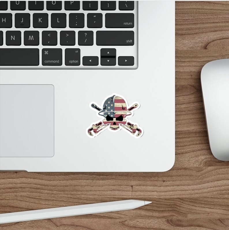 May include: A sticker with a skull wearing a hard hat with the American flag on it. The skull is holding two crossed wrenches.
