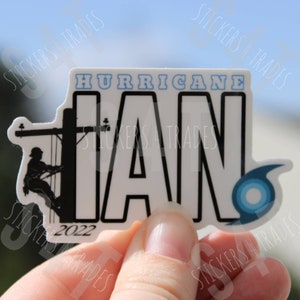 May include: A white sticker with black text that reads "Hurricane Ian 2022". The sticker features a silhouette of a lineman working on a power line.