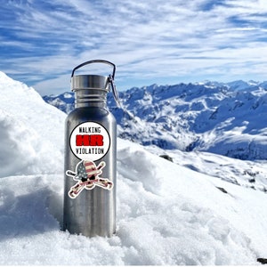 May include: A stainless steel water bottle with a white sticker that says "Walking Violation" and a red, white, and blue skull and crossbones sticker. The bottle is sitting on a snowy mountain.