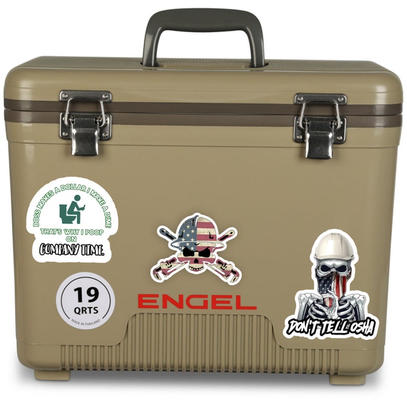 May include: A tan-colored Engel cooler with a 19 quart capacity. The cooler has several stickers on it, including one that says "Boss Makes a Dollar I Make a Dime That's Why I Poop on Company Time", another with a skull and crossbones with an American flag and the words "Don't Tell OSHA", and a third with a skull and crossbones with a hard hat and the words "Don't Tell OSHA".