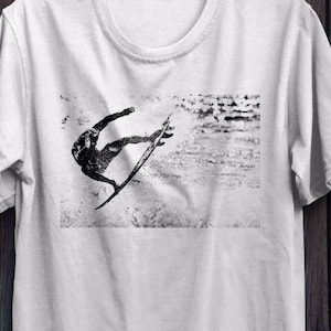 May include: White t-shirt with a black and white graphic print of a surfer riding a wave.