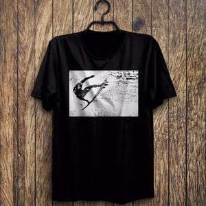 May include: Black t-shirt with a graphic print of a person surfing a wave. The graphic is in black and white.