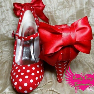 May include: Red and white polka dot heels with a large red satin bow on the front. The heels are on a white surface.