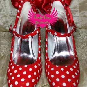 May include: A pair of red and white polka dot shoes with a red bow on top. The shoes have a white strap and a silver insole.