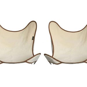 May include: Two butterfly chairs with cream-colored canvas seats and brown trim. The chairs have a distinctive butterfly wing shape, with a curved top and angled bottom. The frames are a dark color.