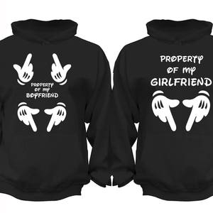 May include: Two black hooded sweatshirts with white Mickey Mouse-style hands and text. One sweatshirt says "Property of my Boyfriend" and the other says "Property of my Girlfriend".