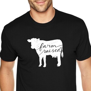 May include: A black t-shirt with a white silhouette of a cow and the text "farm raised" printed on the front.