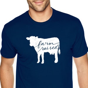 May include: A navy blue t-shirt with a white silhouette of a cow and the text "farm raised" printed on the front.