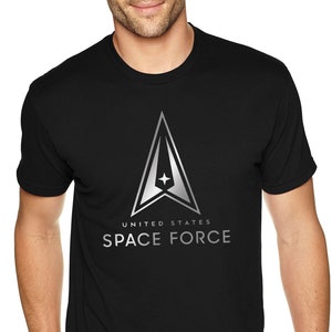 Könnte beinhalten: Schwarzes T-Shirt mit einer silbernen Grafik des Logos der United States Space Force. Das Logo zeigt einen Deltaflügel mit einem Stern in der Mitte und dem Text "UNITED STATES SPACE FORCE".