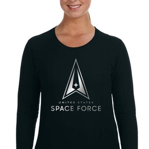 Puede incluir: Camiseta negra de manga larga con un gráfico plateado del logotipo de la Fuerza Espacial de los Estados Unidos. El logotipo presenta un delta estilizado con una estrella en su interior y el texto "UNITED STATES SPACE FORCE".