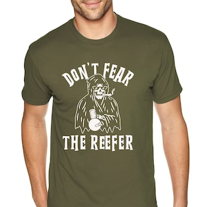 May include: Olive green t-shirt with the text "DON'T FEAR THE REEFER" above and below a white graphic of a grim reaper smoking a cigarette and holding a microphone.